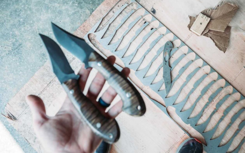 Two knives in hand and a third knife resting on scrap metal